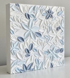 a white and blue tile with leaves on the side, sitting on top of a table