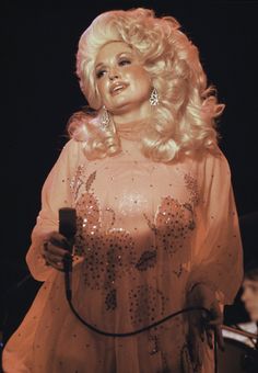 a woman with blonde hair wearing a dress and holding a microphone in her right hand