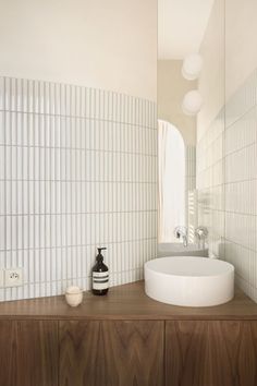 a white sink sitting on top of a wooden counter next to a bathroom mirror and light fixture