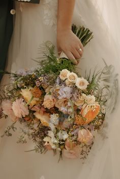 a bride holding a bouquet of flowers in her hand and wearing a wedding ring on her finger