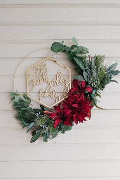 a christmas wreath hanging on the side of a white wall with red flowers and greenery