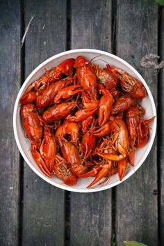 a white bowl filled with cooked craws sitting on top of a wooden table