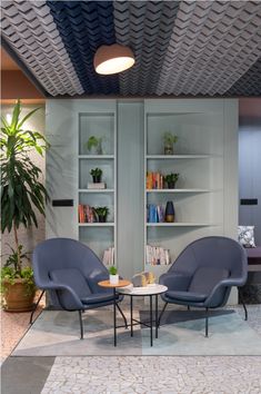 two blue chairs sitting next to each other in front of a book shelf filled with books