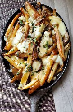 french fries with cheese and herbs in a black bowl on a tableclothed cloth