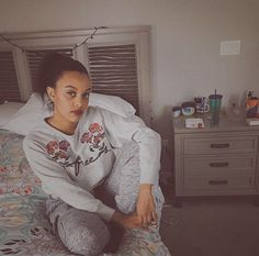 a woman sitting on top of a bed next to a night stand and dressers