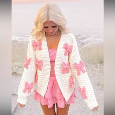 a woman walking down the street wearing a pink and white crochet sweater with flowers on it