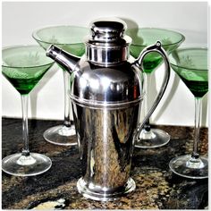 three martini glasses and a silver pitcher sitting on a marble counter with green liquid in them