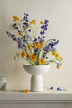 a white vase filled with yellow and blue flowers