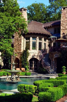 a large house with a fountain in front of it and lots of greenery around the yard