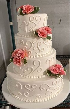 a three tiered cake with pink roses on top is sitting on a cooling rack