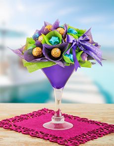 a purple vase filled with chocolates and flowers on top of a pink place mat