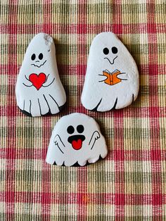 three rocks painted to look like ghost faces on a plaid tablecloth with red and white checkered cloth