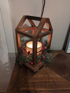 a wooden lantern with a lit candle inside on a table next to a christmas wreath