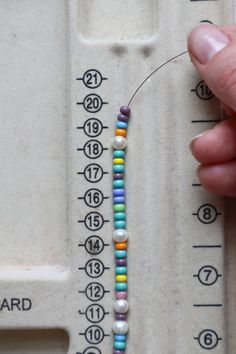 a person is holding a beaded necklace in front of a measuring scale with numbers on it