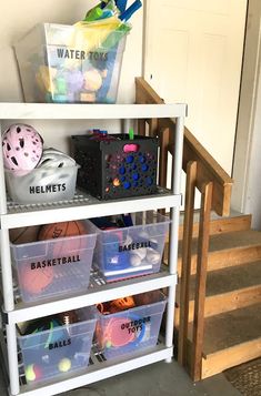 a white shelf filled with plastic bins next to a stair case full of toys