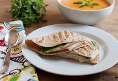 a white plate topped with a cut in half sandwich next to a bowl of soup