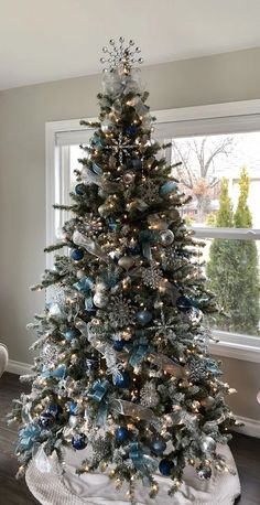 a decorated christmas tree with blue and silver ornaments in a living room window sill