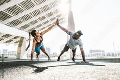 two people doing push ups on the ground in front of a large building with a sky background