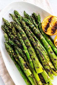 asparagus spears on a white plate with lemons and orange slices in the background