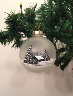 an ornament hanging from a christmas tree with a house in the snow on it