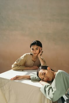 two women laying on a bed with their heads resting on the table and looking at the camera