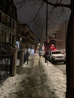 a snowy street at night with cars parked on the side and buildings in the background