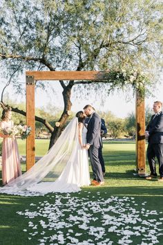 a bride and groom are kissing under an arbor at their outdoor wedding in the park