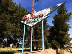 an old neon sign that is on the side of a road in front of some trees