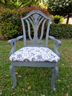 an old chair with a blue upholstered seat is sitting in the grass outside