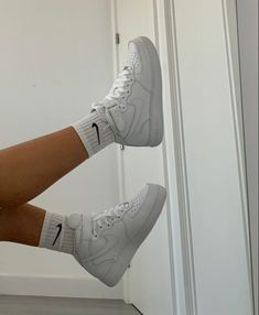 a woman's legs with white nike shoes hanging off the side of a door