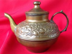 a metal tea pot sitting on top of a red cloth