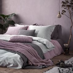 a bed covered in pink and grey blankets next to a window with potted plants