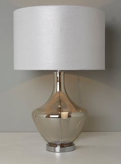 a glass table lamp with a white shade on the base and a light bulb attached to it