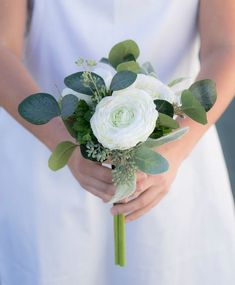 a bride holding a bouquet of white flowers and greenery in her hands, close up