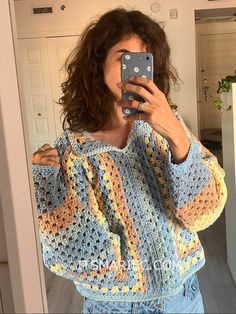 a woman taking a selfie in front of a mirror wearing a crocheted sweater