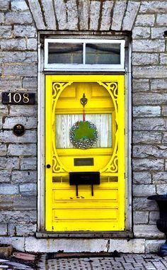 a yellow front door with a window and number on the side of a brick building