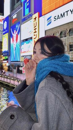 a woman eating food in the middle of a busy city street with billboards behind her