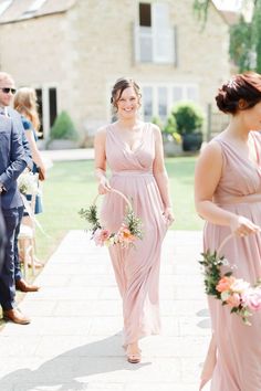 the bridesmaids are walking down the aisle with their bouquets in hand and one is wearing a pink dress