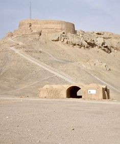 an open tunnel in the middle of a desert with a rock formation behind it and a radio tower on top