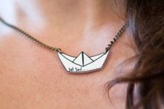 a woman wearing a necklace with a paper boat on it