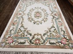 a white rug with flowers and fringes on top of wooden floor next to wall