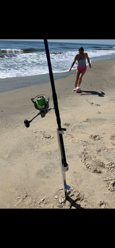 a woman walking on top of a sandy beach next to the ocean holding a fishing pole