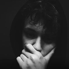 a young man covers his face with his hands as he stares into the camera, in black and white