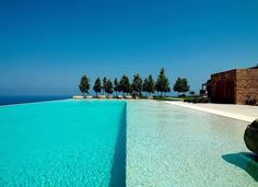 an empty swimming pool in front of the ocean with lounge chairs and trees on either side