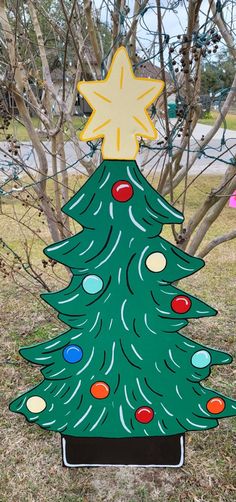 a cardboard christmas tree with lights on it in front of some bare trees and grass