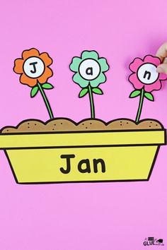 a hand is holding up a flower pot with flowers in it and the word jan on it