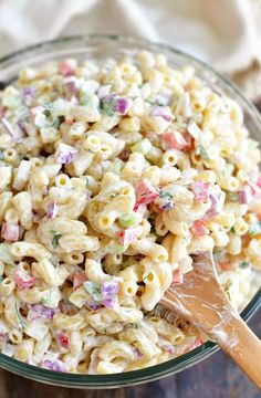 macaroni salad in a glass bowl with a wooden spoon