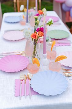 the table is set with pink and white plates, silverware, and flowers in vases