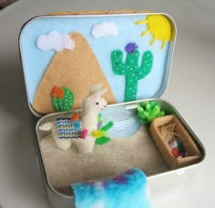 an open tin can filled with felt animals and cactuses on the table next to it