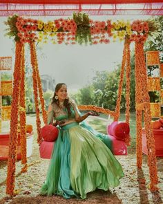 a woman is sitting on a swing with flowers around her and wearing a green dress